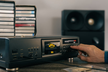 Closeup photo of man pressing play on vintage stereo cassette recorder. Room setup with vintage audio gear, including a cassette recorder, emphasizing nostalgia and music enjoymentの写真素材
