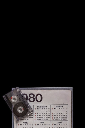 Old paper calendar of 1980 and audio tape cassette isolated on black background. Nostalgic 80s calendar with an audio cassette, perfect for retro-themed contentの写真素材