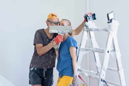 Young family couple having fun while doing renovation and plasterwork. Man and woman enjoying a...