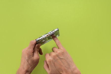 Closeup of man rewinding cassette magnetic tape with finger on green background, Close-up of a...