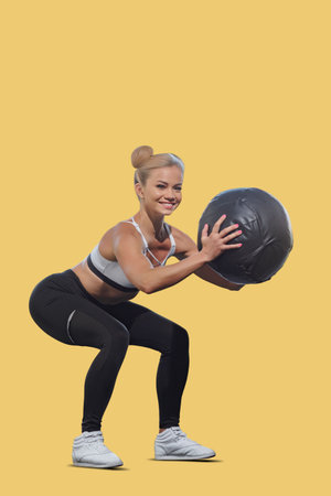 Beautiful fit athletic girl doing fitness training with medicine ball, Fitness girl in black attire, isolated against a colored backdrop, perfect for active lifestyle and workout visualsの写真素材