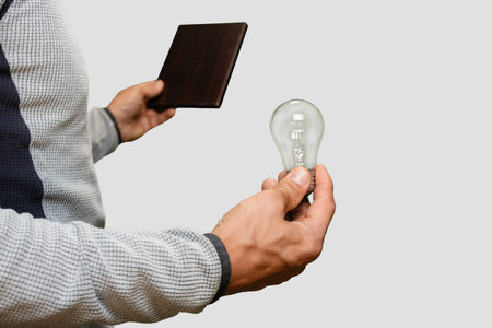 Male electrician working with tablet to measure the voltage and install light bulb, Energy awareness: man holding an incandescent light bulb, counting electricity usage and monitoring consumptionの写真素材