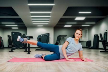 Young fit sporty active girl stretching legs muscles in gym. Fitness enthusiast: girl working out solo in a contemporary gym spaceの写真素材