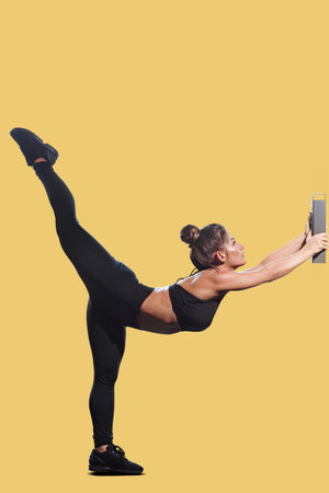Slim athletic sporty young woman stretching legs with block on yellow background, Fitness girl posing on a colored background, ideal for promoting workout routines and active lifestylesの写真素材