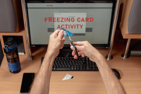 Upset man using online banking service and cutting his credit card with scissors. Account freeze alert on computer monitor, male client concerned about payment card freezeの写真素材