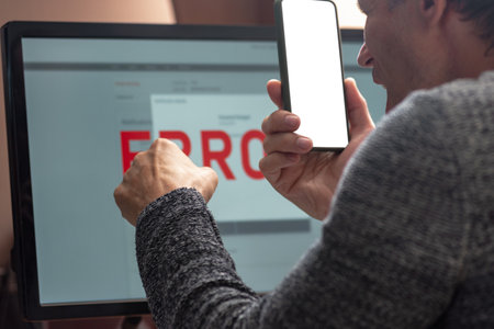 Angry man having computer app crash error calling to tech support. Close-up from behind of a man facing a computer error, displaying a range of emotions while reviewing critical data on the screenの写真素材