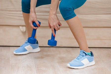 Closeup photo of female athlete doing squatting with dumbbellsの写真素材