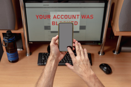 Man faced with problem while paying online and calling to bank tech support. Mans hands shown as he receives account blocking alert on monitor, bad news displayed on screenの写真素材