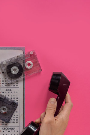 Man with old telephone, paper calendar and retro audio cassettes feeling sad for the past times. Audio cassette and vintage 80s calendar, evoking memories of retro timesの写真素材