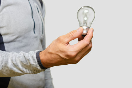 Closeup photo of young man holding lighting bulb on white background, Energy-saving concept: man with an incandescent light bulb, highlighting recycling and replacement effortsの写真素材