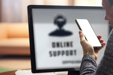Young man needing online help with setting up device talking with tech support. Man interacting with online support through a computer, showcasing seamless communication, from behind the monitorの写真素材