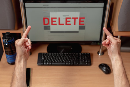Angry man showing two middle fingers to computer screen with text delete, Male user reacting with anger as data deletion occurs on screen, account removal in progressの写真素材