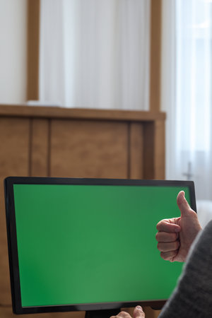Closeup of man using computer and gesturing thumb-up over successful work. Man showing a range of emotions in front of a chromakey monitor, symbolizing the challenges of navigating computer problemsの写真素材