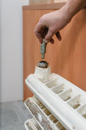 Closeup of man dismantling and repairing old cast heating radiator in house. Rusty cast iron radiator being removed for restoration, home heating system renovation in progressの写真素材
