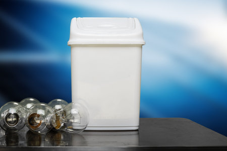 Old incandescent lamps thrown into trash for recycling. Disposing of an incandescent lamp into a recycling bin, against a gradient blue background, showcasing environmental consciousnessの写真素材