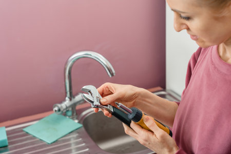 Closeup photo of handy woman with wrench fixing kitchen faucet, Funny portrait of a girl plumber with an adjustable wrench, confident and ready for workの写真素材