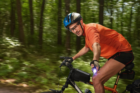 Young athletic male cyclist using ultrasonic dog repeller for protection. Male cyclist prepared with repellent device, avoiding dog encounter on dirt roadの写真素材