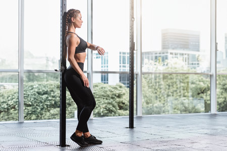 Beautiful young fitness woman in black sportswear posing near big window in modern gym, Black clothes, crossfit zone, gym with glass windows, girl workoutの写真素材