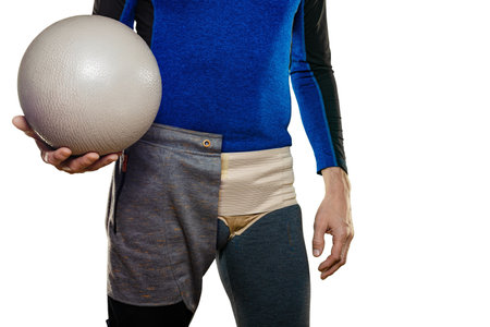 Closeup of man wearing inguinal hernia belt while doing exercises with ball. Fit man in partial...