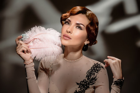 Elegant gorgeous woman with cold finger wave hairstyle and feather. Studio portrait of retro girl holding feather fan, wearing sheer blouse and classic hairstyleの写真素材