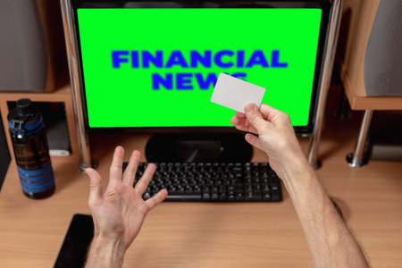 Man with credit card doing online shopping after receiving money. Financial news on screen, man with emotional response, keyboard visibleの写真素材