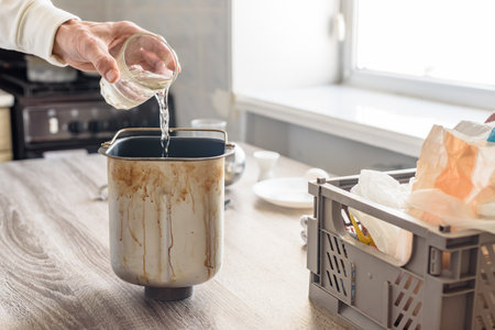 Closeup photo of man pouring glass of water into bread making pan. Fresh bread dough rising in a glass form with water nearby for home bakingの写真素材