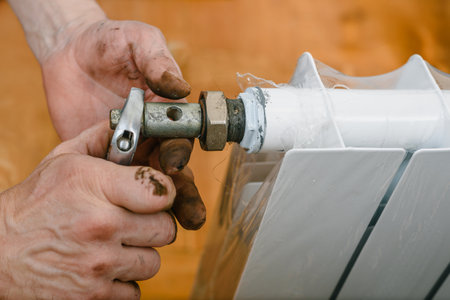 Closeup of male plumber fixing heating radiator with wrench. Heating system maintenance, new battery unpacked and ready for installation in apartmentの写真素材