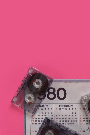 Old audio cassettes tape together with calendar from the 1980s on bright pink background. Retro 80s calendar alongside an audio cassette, perfect for nostalgic designsの写真素材