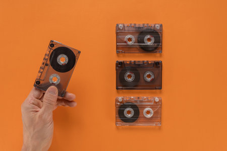 Male music lover showing vintage music audio cassettes tape of 80s on orange background. Hand gripping a retro audio cassette against a simple flat backgroundの写真素材