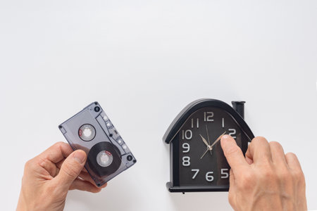 Closeup of man with audio cassette and old watch reliving musical memories. Hand gripping audio cassette and showing a watch, symbolizing a nostalgic return to the past and retro memoriesの写真素材