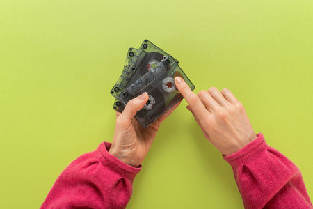 Woman holding retro 80s audio cassettes on green background. Flat background with hands and a retro...