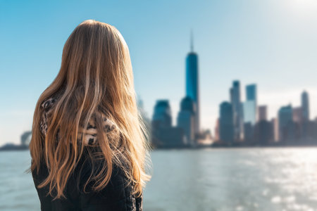 Back view of attractive young blonde woman in City. Woman with long blonde hair overlooking city skyline and river on a clear sunny dayの写真素材