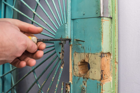 Closeup of man chiseling groove in door leaf for lock installation. Worker carving out door frame with tool, preparing area for lock replacementの写真素材