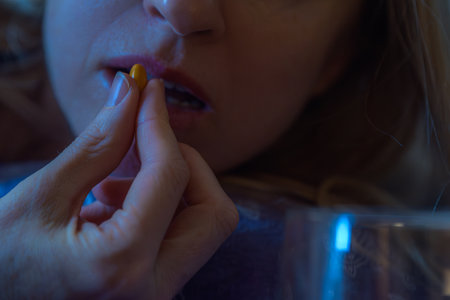 Closeup of young woman taking vitamin for treatment body strong. Woman taking yellow pill with water, closeup of hand and lips in low light, healthcare conceptの写真素材