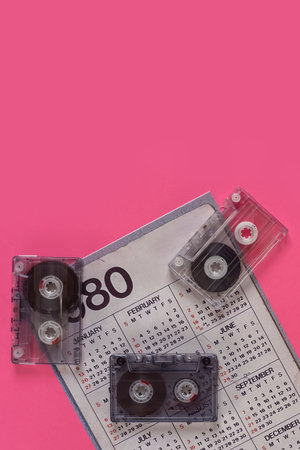 Old cassette tapes with 1980 calendar isolated on pink background. Audio cassette and calendar from the 80s, highlighting classic retro nostalgiaの写真素材