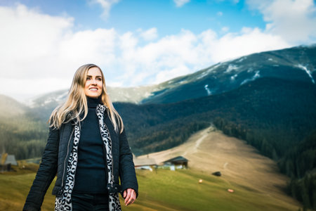 Pretty happy woman walking down mountain path on spring sunny day. Traveler admiring panoramic snowy peaks and green pine woods on bright afternoonの写真素材