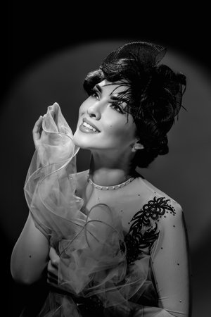 Black and white portrait of beautiful woman with elegant evening makeup and hair, wearing retro hat. Girl in retro style with Hollywood wave hairstyle posing like actress in black and white portraitの写真素材