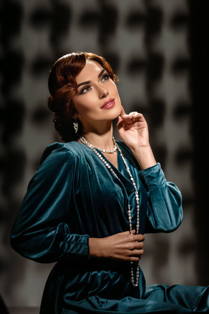 Vintage styled woman with perfect make up and hairstyle wearing necklace. Retro fashion girl with stylish dress, fan, feathered veil, and headdress posing in studio portraitの写真素材