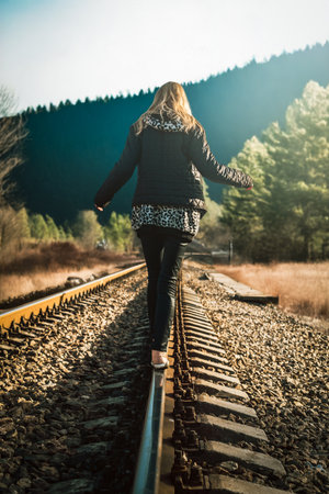 Young blonde walking on train tracks in mountainous area on sunny day. Woman walking on railway track near mountains, enjoying freedom, nature and balance on sunny day.の写真素材