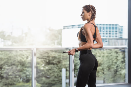 Full length of young beautiful woman with well trained body wearing black sportswear posing in front of window in gymの写真素材