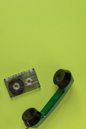 Retro audio tape cassette and old rotary telephone isolated on green background. Retro audio...