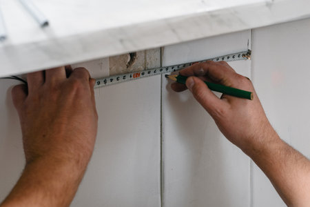 Male hands measuring surface of plastic board for wall. Worker using a level tool to check vertical...