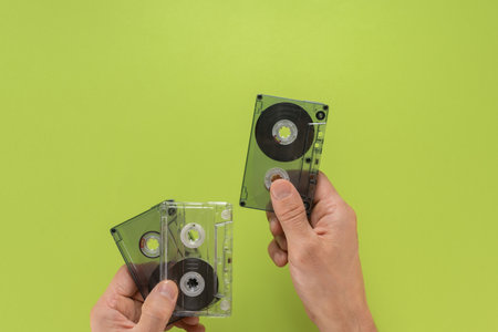Closeup of male music lover showing vintage audio cassettes with greatest hits. Hand displaying audio cassette, flat background, open copy space. Perfect for nostalgic and vintage designsの写真素材