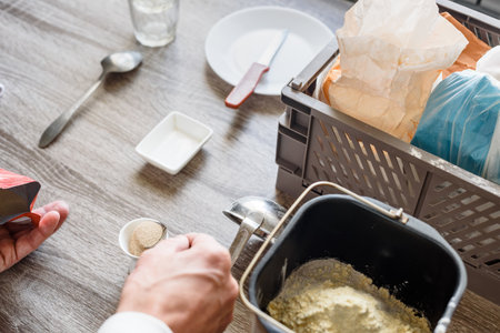 Closeup photo of man making homemade bread, adding yeast to the dough. Home bread baking with flour,...