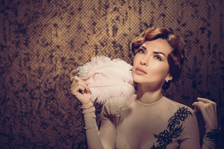 Beautiful young retro style woman posing with feather. Classic style model in sheer dress with soft...