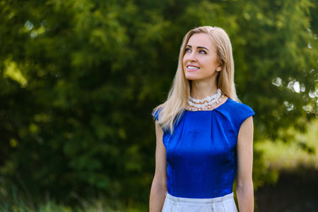 Attractive young blonde woman enjoying her time outside in warm sunny weather. Woman looking up with inspired expression, elegant fashion in summer nature settingの写真素材