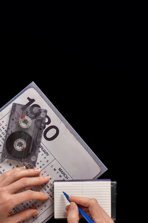 Woman making song list of her favorite music of 80s. Vintage audio cassette with a calendar from the 1980s, illustrating a nostalgic look back at past decadesの写真素材