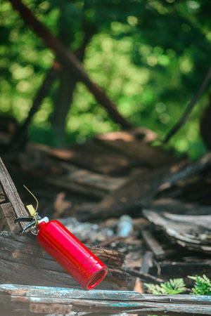 Ruins of wooden house after fire has been extinguish. Abandoned extinguisher in ruins, reminder of...