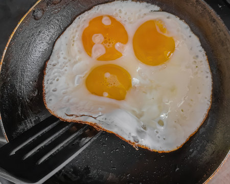 Closeup photo of three fried eggs in iron pan. Fried eggs in skillet being lifted with spatula, homemade breakfast prepの写真素材