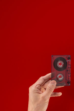 Man holding vintage old audio cassette with music of 90s. Audio cassette in hand, flat backdrop, open copy space. Perfect for retro-themed graphicsの写真素材